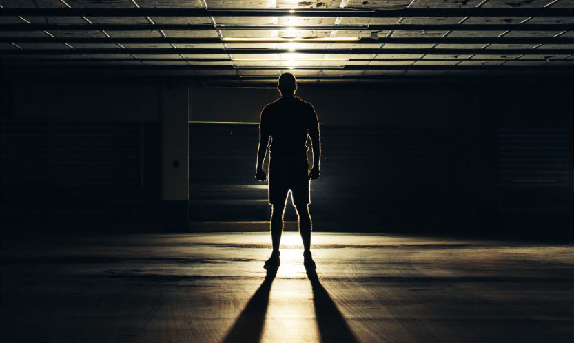 Man standing alone in the dark with light in front of him.